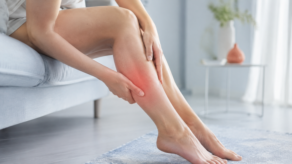 Soigner jambes lourdes Femme assise massant son mollet douloureux en rouge, signe de jambes lourdes et de mauvaise circulation