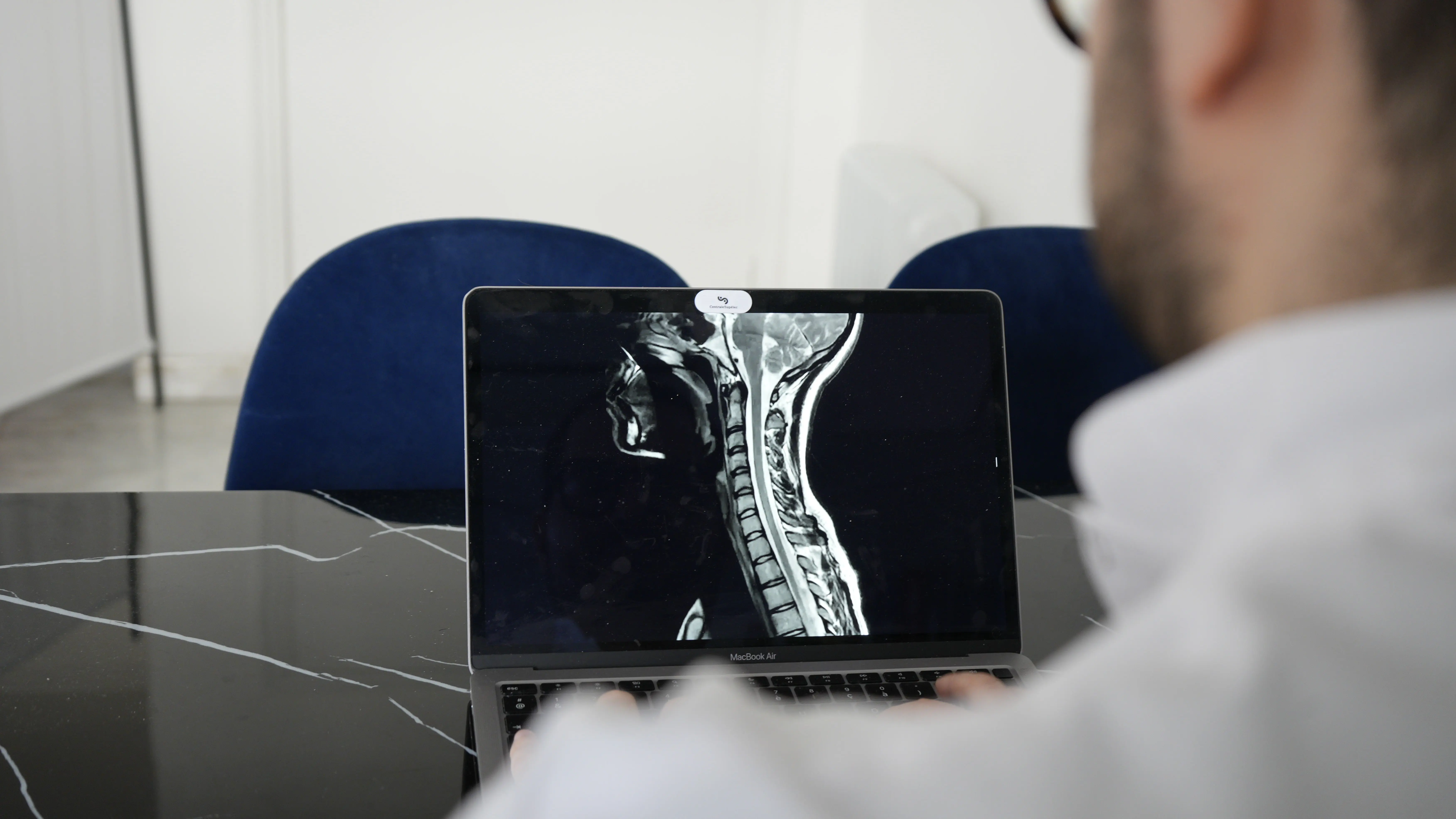 Ostéopathe à Nice analysant l'IRM des cervicales d'un patient sur son ordinateur portable en cabinet