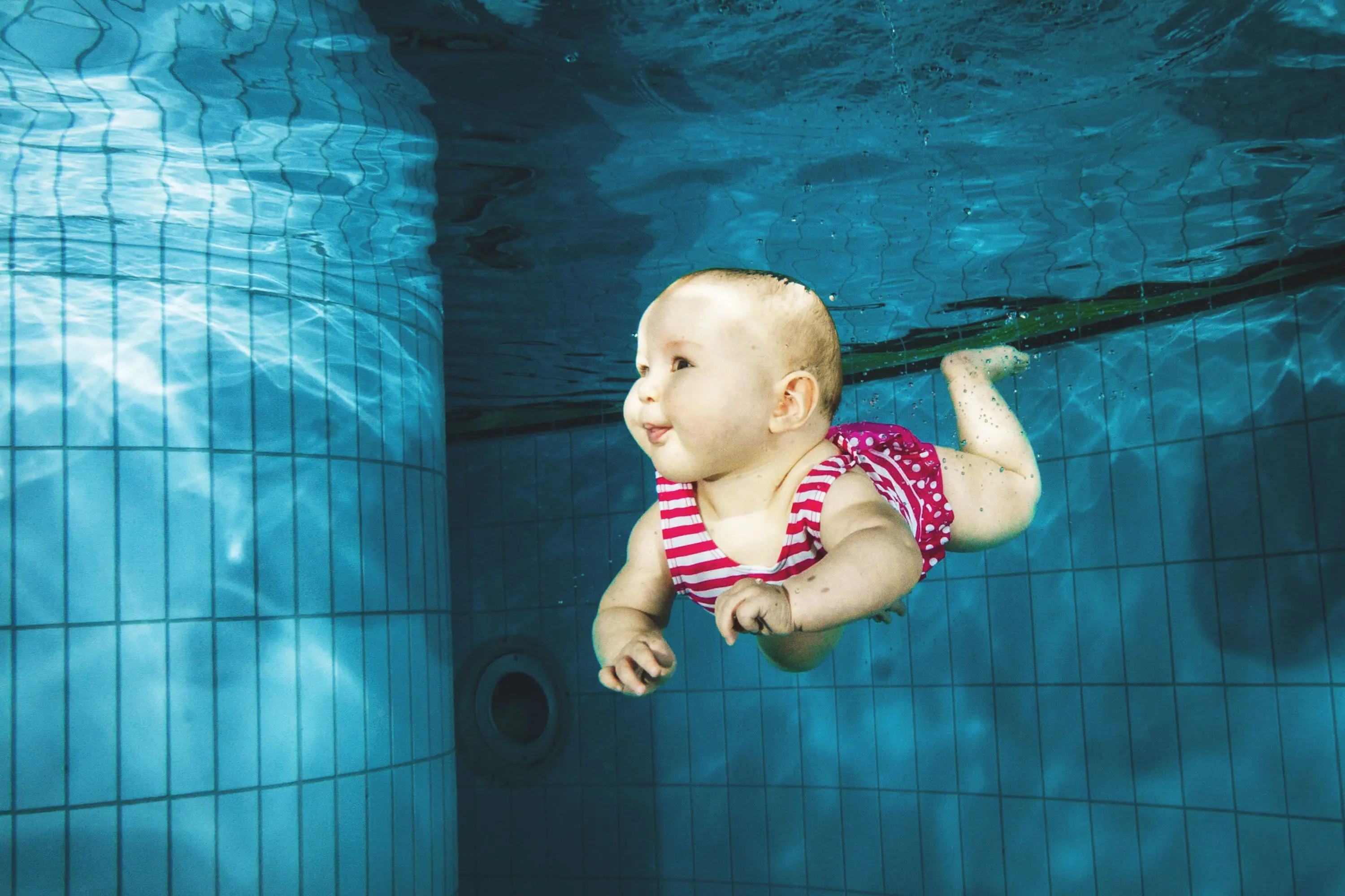 Bébé souriant nageant sous l'eau en piscine, image associée à l'ostéopathie du nourrisson à Nice