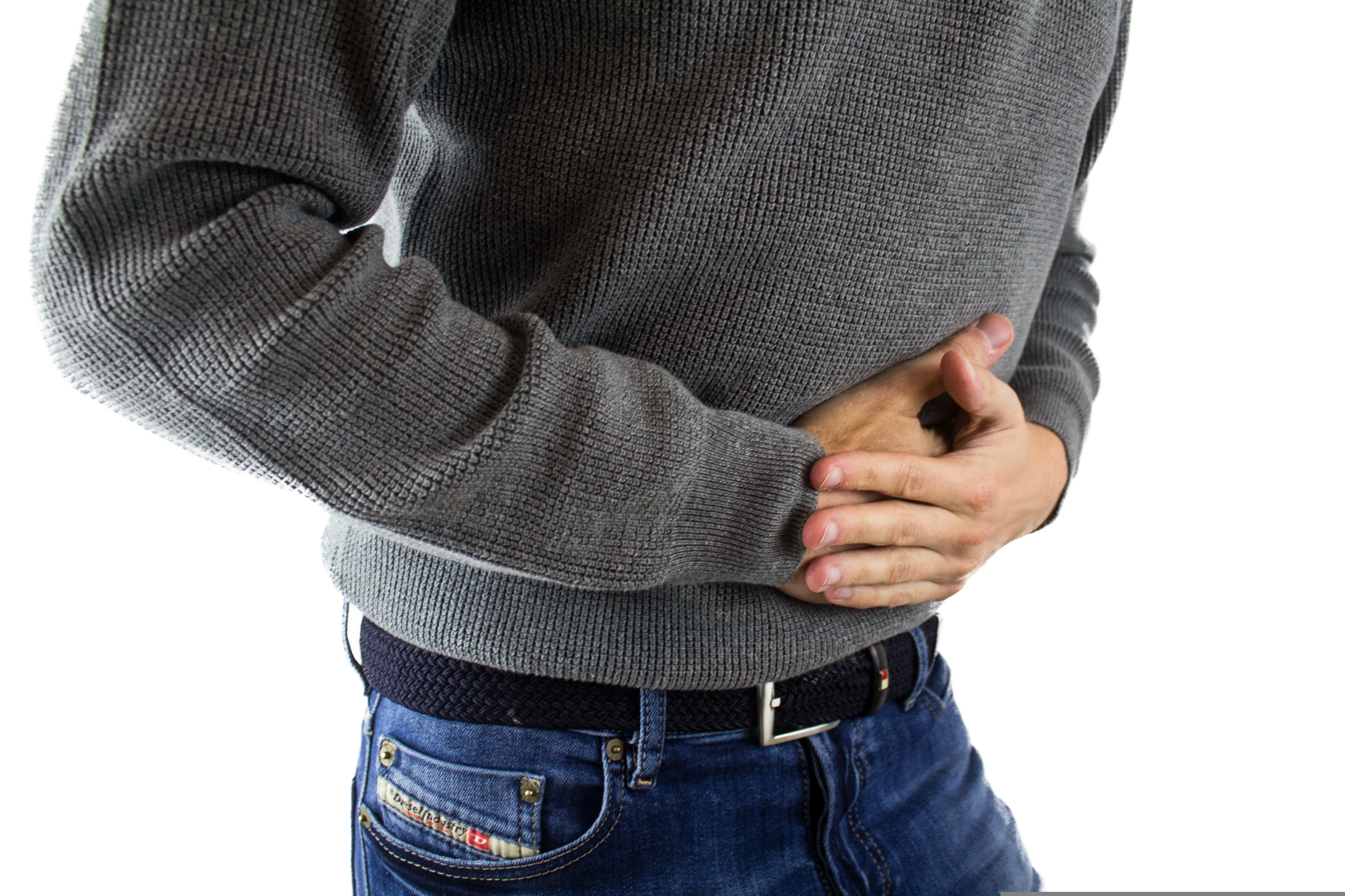 Homme en pull gris se tenant le ventre avec les mains, signe de douleur abdominale et de troubles digestifs